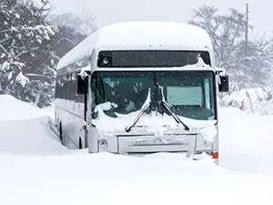 大雪の中で雪山に乗り上げて停車している白い大型バスの正面