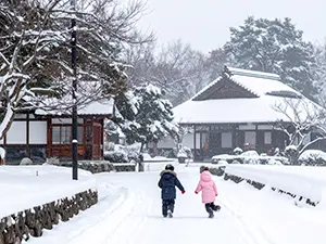 雪の積もった広場を奥に向かって走っていく防寒着を着た二人の子供