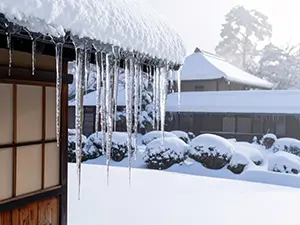 日本家屋の軒先から垂れ下がる多数の鋭い氷柱と雪の庭