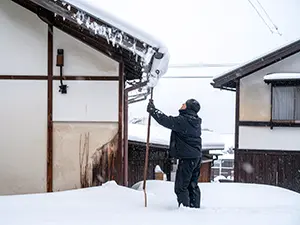 長い道具を使って屋根の雪を落とす防寒着を着た男性