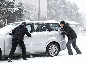 雪道で動けなくなったシルバーの車を後ろから押す二人の男性