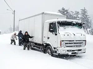 雪道で立ち往生した白いトラックを人力で押している3人の男性作業員