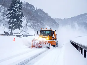 山道の雪を勢いよく横に飛ばしながら走行するオレンジ色の除雪車