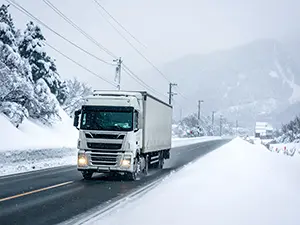 雪の積もった道路を走る白い大型トラックと雪山の風景